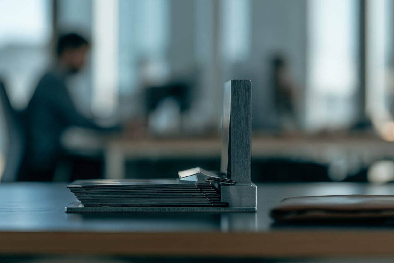 A fanned stack of metal plates on a desk, a colleague working behind.